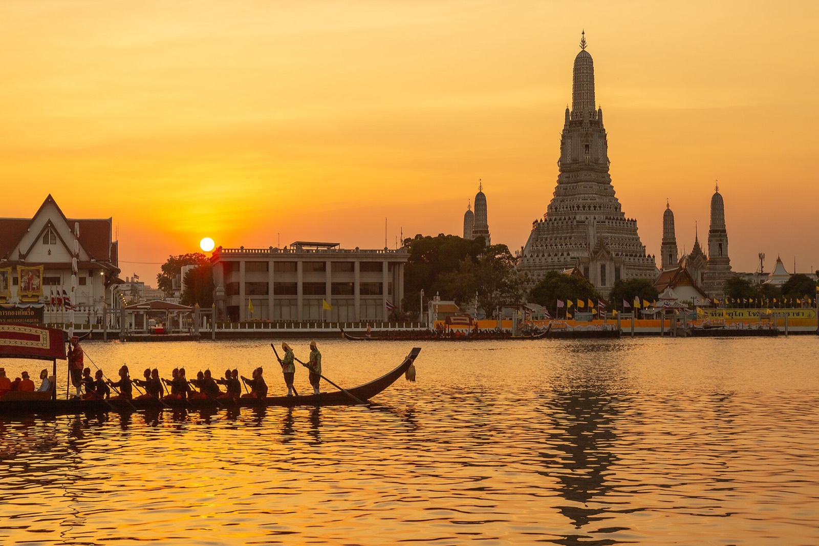 Wat Arun's spires silhouetted at sunset over the Chao Phraya River, Bangkok